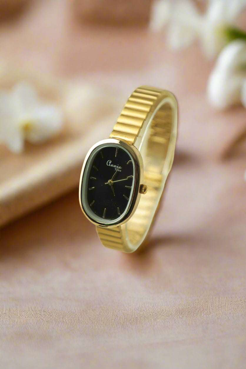 Gold watch with black face on a soft background, featuring the Luxora brand.